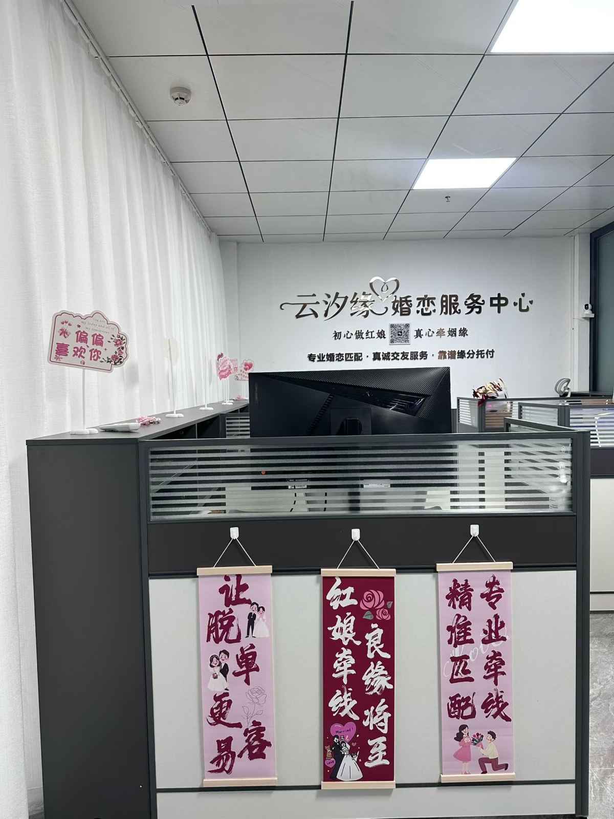 接待前台，背后是品牌形象墙，桌前挂着红娘牵线的祝福挂幅